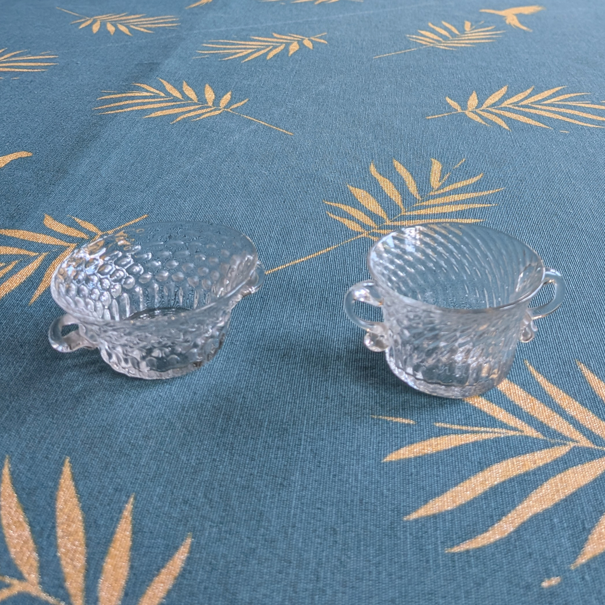 Two small clear textured crystal bowls viewed from the opposite side, with their handles visible.