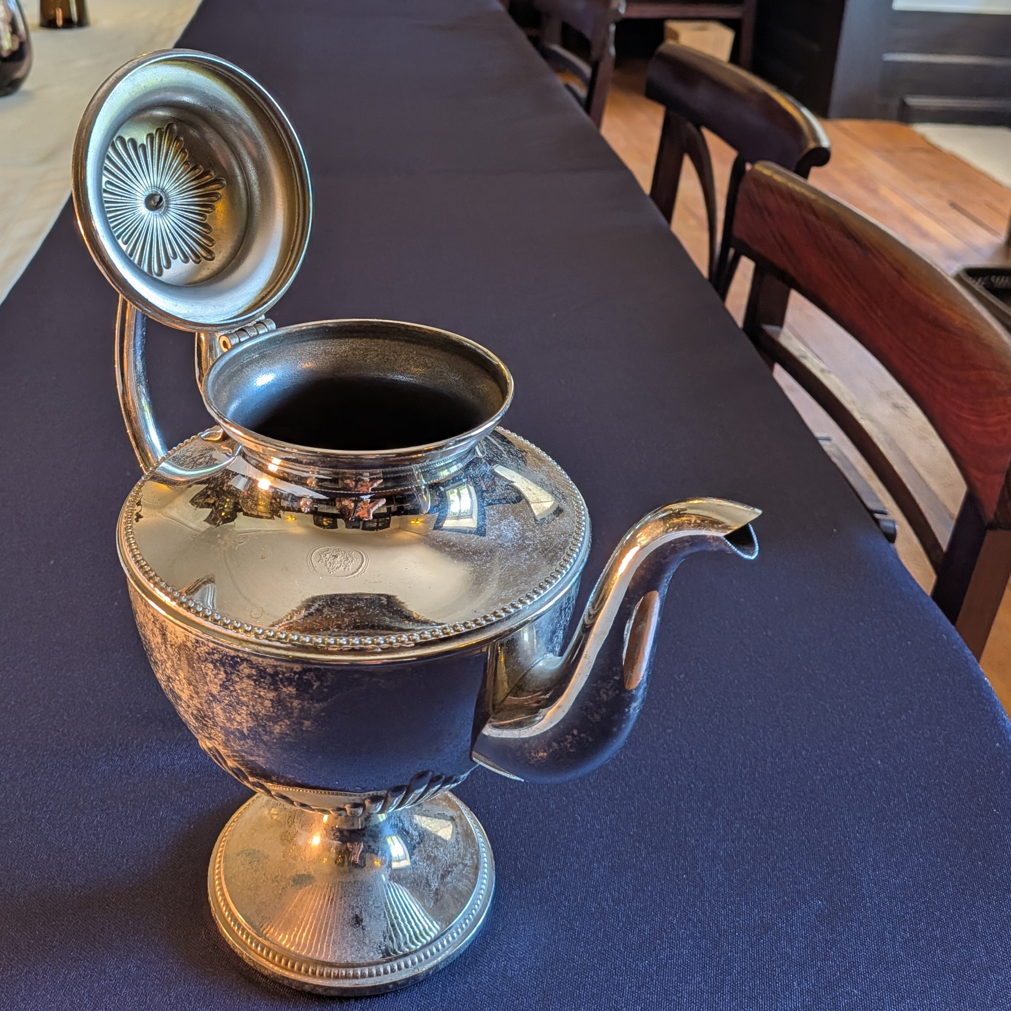 Shorter metal pot with its hinged lid open, showing the opening, lid decoration and surface marks.