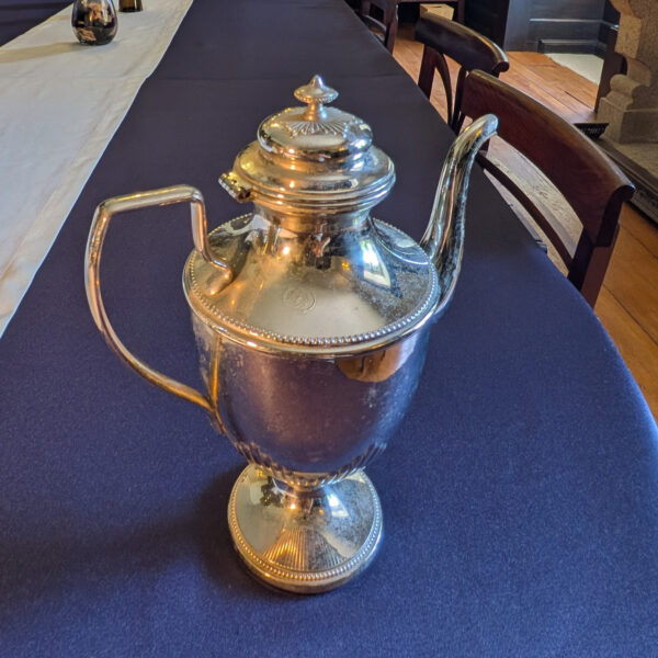 Opposite side of the taller metal pot, showing its handle, long curved spout and visible surface marks.