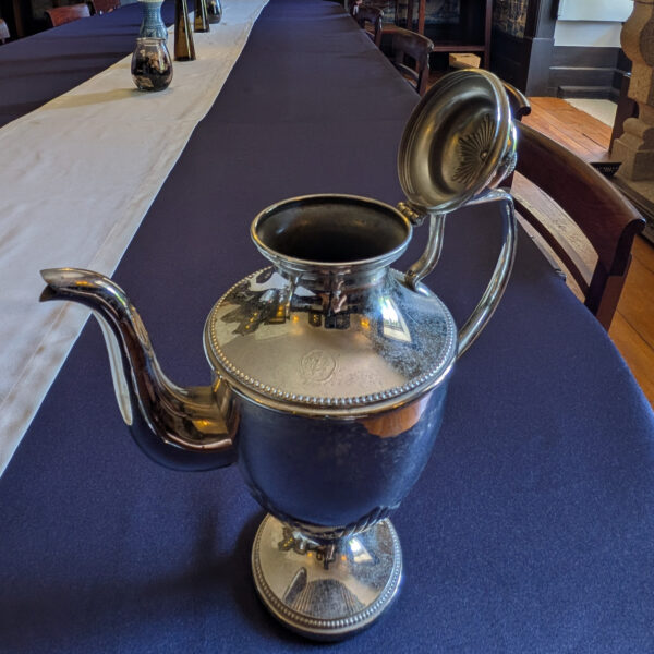 Taller silver-coloured metal pot with its hinged lid raised, showing the opening and underside of the lid.