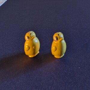Two miniature yellow ceramic chick salt and pepper shakers, shown together with their faces and raised wings.