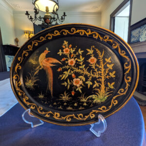 Full front view of an oval black tray with a long-tailed bird, flowers and a gold scrolling border.