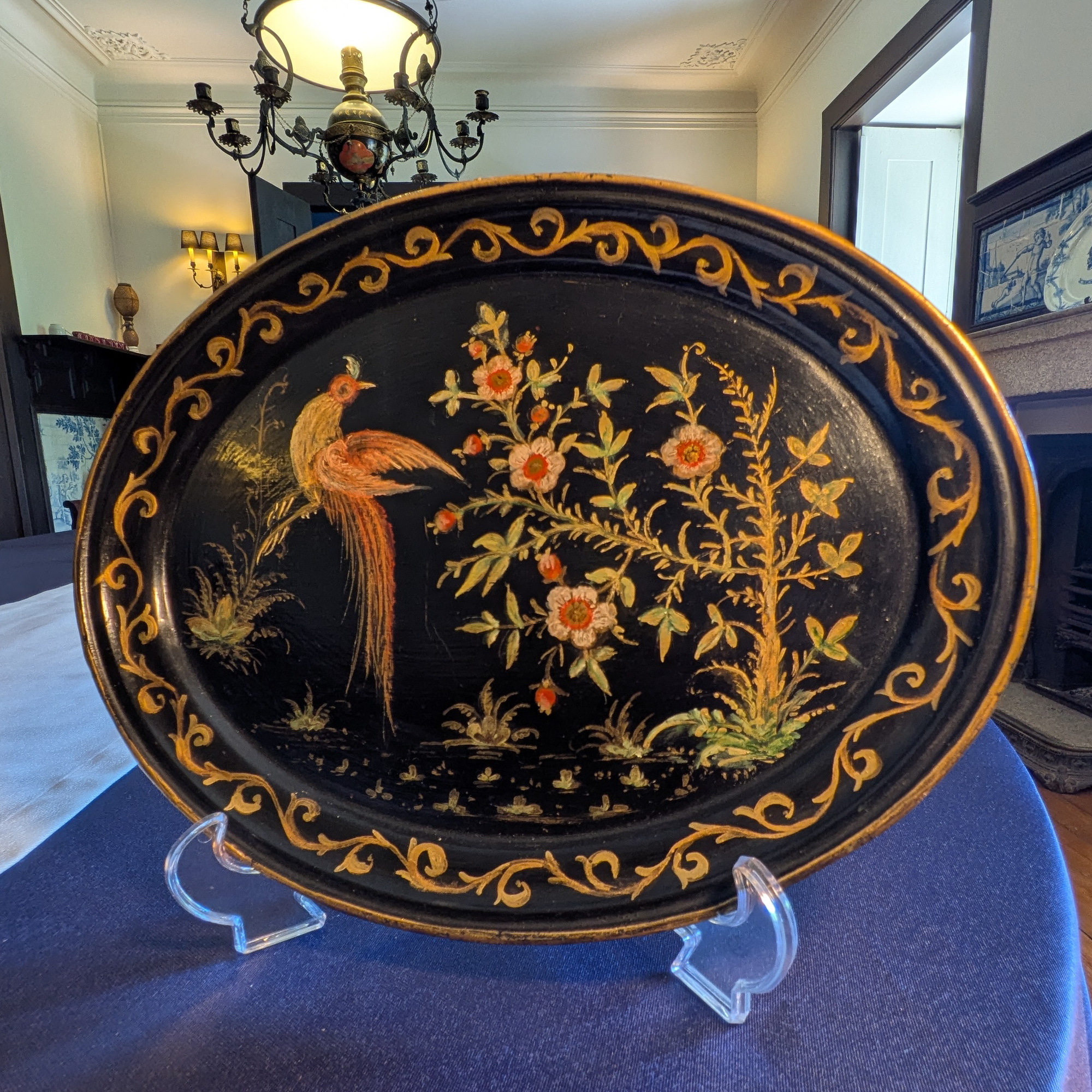 Full front view of an oval black tray with a long-tailed bird, flowers and a gold scrolling border.